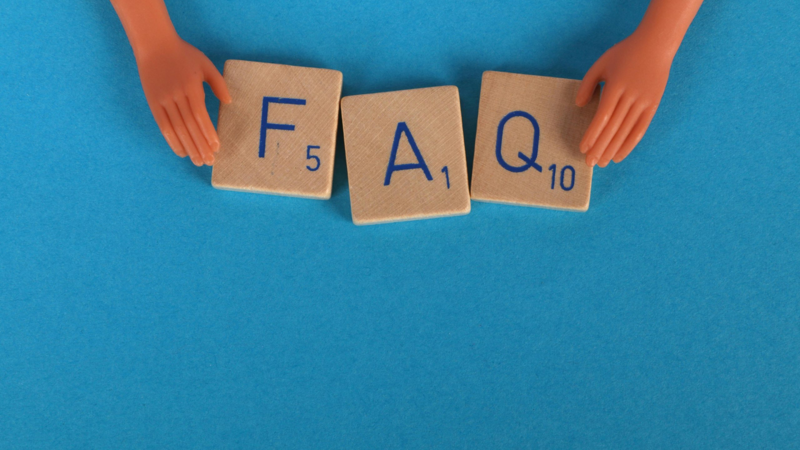 Two plastic doll hands frame three wooden letter tiles spelling out the acronym FAQ (Frequently Asked Questions) on a bright blue background.